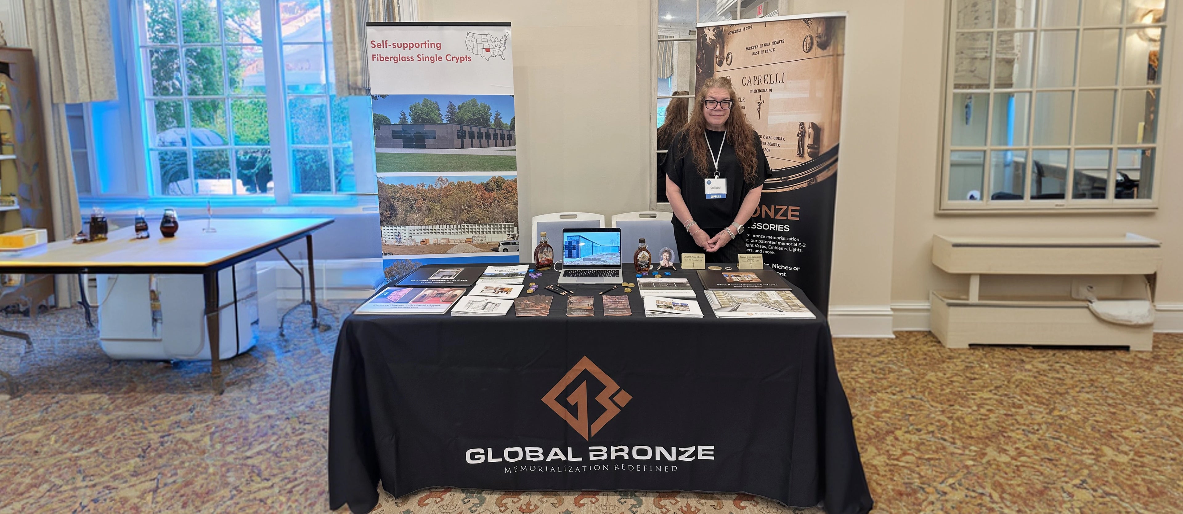 Person standing behind a table with a Global Bronze brand display at an event
